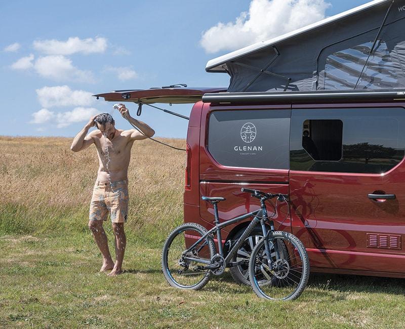 Campeur qui se douche à l'extérieur grâce à la douchette de son van Glénan